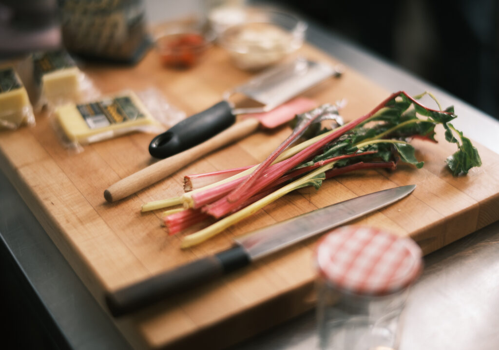 Several stems of Swiss Chard laid on a cutting board next to a knife and several other blurry food items
