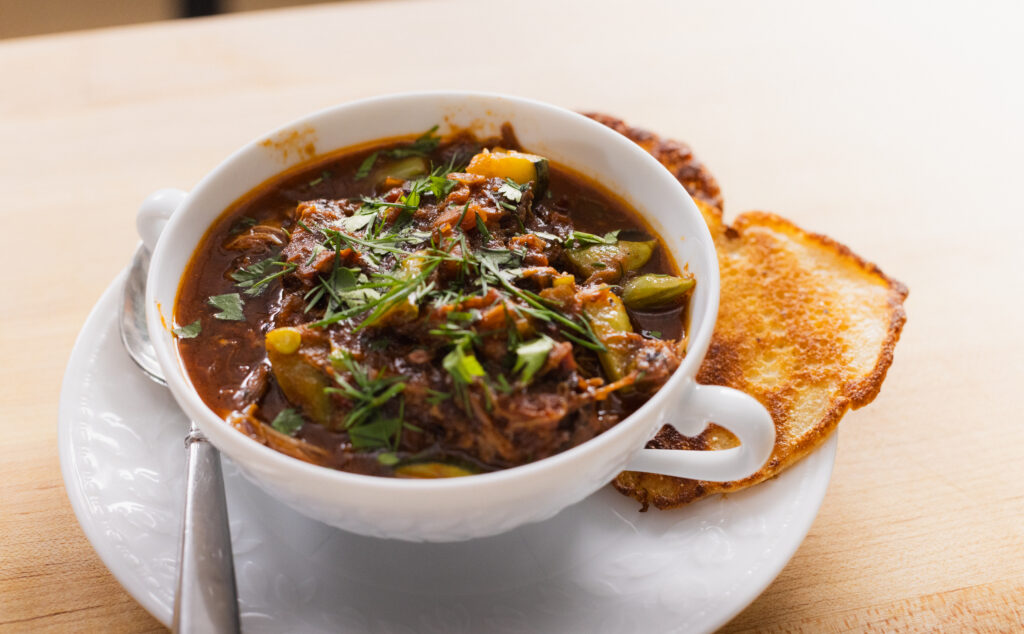 A bowl of burgoo with a hoe cake on the side